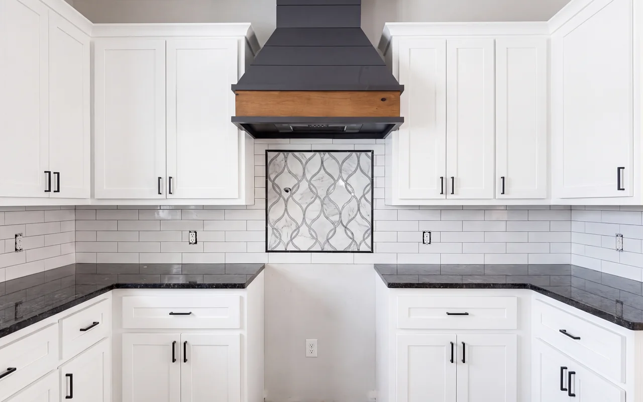 White subway backsplash with marble mosaic feature panel under a black and wood range hood