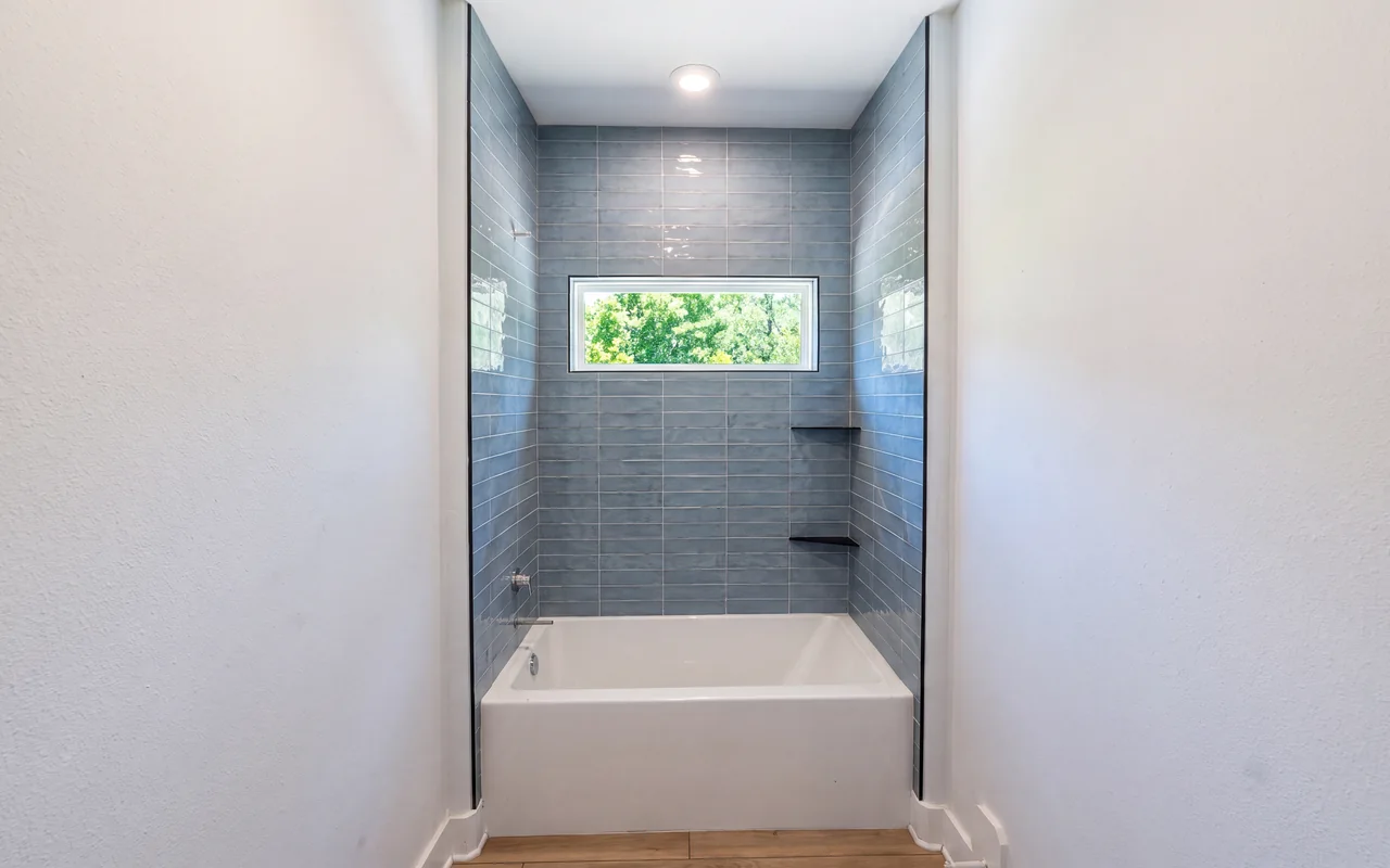 Blue-gray subway tile tub surround with a picture window and black corner shelves